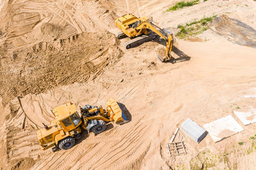 yellow earthmover and excavator doing ground works during road construction. aerial view