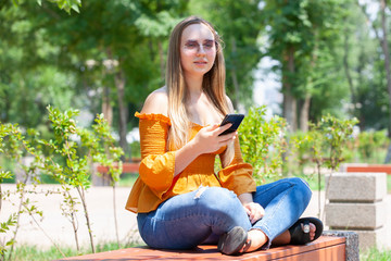 Close-up portrait of glamorous girl in glasses talking on phone. Outdoor portrait a blonde young woman talking by her smartphone.