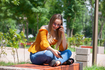 Close-up portrait of glamorous girl in glasses talking on phone. Outdoor portrait a blonde young woman talking by her smartphone.