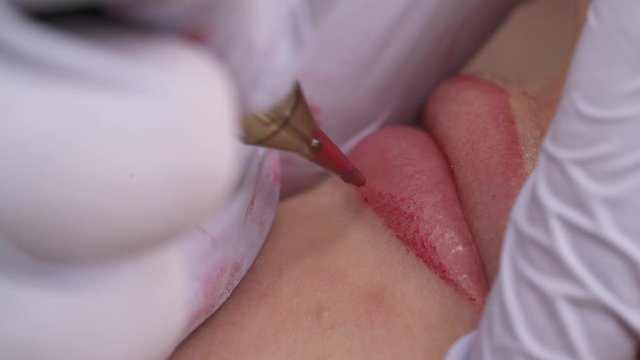 Close-up of patients lips during the procedure of lip blushing with tattoo machine. Permanent cosmetics. Beauty concept