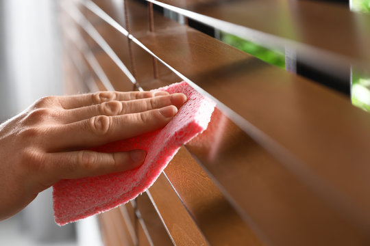 Man wiping window blinds with rag indoors, closeup. Space for text