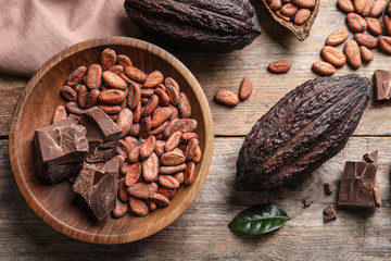 Flat lay composition with cocoa beans, chocolate pieces and pods on wooden table