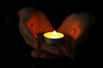 Woman holding burning candle in darkness, closeup