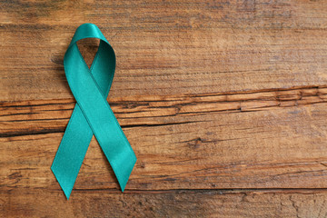 Teal awareness ribbon on wooden background, top view with space for text. Symbol of social and...