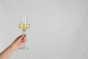 Woman holding glass of white wine on light background, closeup. Space for text