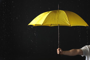 Man holding yellow umbrella under rain against black background, closeup
