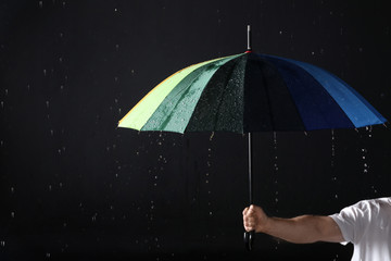 Man holding color umbrella under rain against black background, closeup
