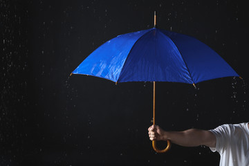 Man holding blue umbrella under rain against black background, closeup