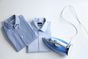 Iron with clean shirts on light background, top view