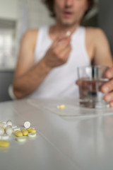 A man holds a glass of water, going to drink pills and tablets lying on the table. Illness, malaise, cold, ache. Front view. Vertical. Close-up