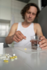 A man holds a glass of water, going to drink pills and tablets lying on the table. Illness, malaise, cold, ache. Front view. Vertical