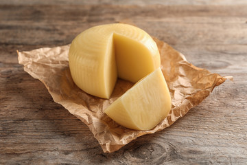 Parchment paper with cut wheel of delicious cheese on wooden table