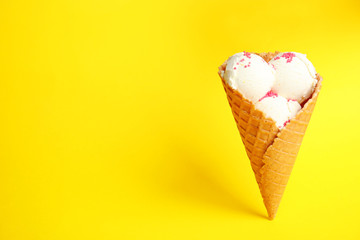 Delicious vanilla ice cream in wafer cone on yellow background. Space for text
