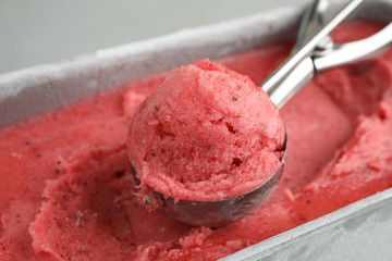 Container with delicious pink ice cream and scoop, closeup
