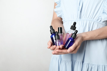 Woman holding bottles of essential oil on light background, closeup. Space for text