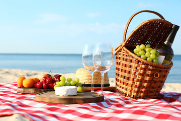 Checkered blanket with picnic basket and products on sunny beach - obrazy, fototapety, plakaty