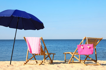 Empty wooden sunbeds and beach accessories on sandy shore