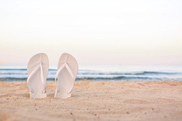 White flip flops on sand near sea, space for text. Beach accessories