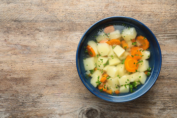 Bowl of fresh homemade vegetable soup on wooden background, top view. Space for text