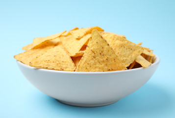 Bowl of tasty Mexican nachos chips on light blue background