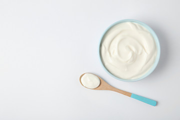 Fototapeta na wymiar Bowl of sour cream and wooden spoon on white background, top view