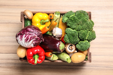 Crate with different fresh vegetables on wooden background, top view