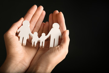 Woman holding figure of family in hands on black background, closeup. Space for text