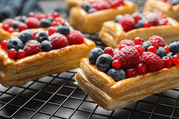 Cooling rack and fresh delicious puff pastry with sweet berries on grey table, closeup