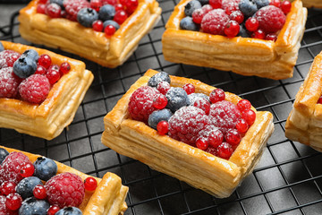 Cooling rack and fresh delicious puff pastry with sweet berries on grey table, closeup