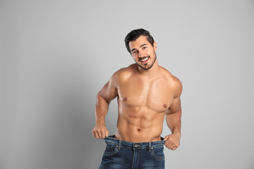 Young man with slim body in old big size jeans on grey background