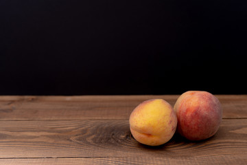 Two juicy ripe sweet peaches lie on a wooden table on a black background. Fruits for diet, healthy eating and lifestyle. Close-up