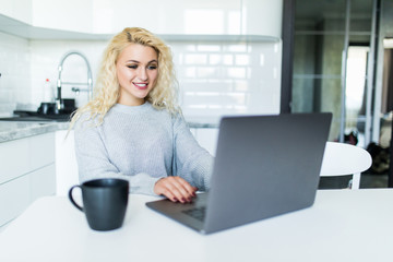 Fototapeta premium Young woman with coffee cup and laptop in the kitchen at home