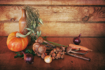 Rural still life of vegetables. On a wooden table is pumpkin mushrooms Armillaria onions carrots parsley and a knife. Wooden background.