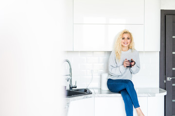 Happy blonde woman drinking tea in the kitchen at home.