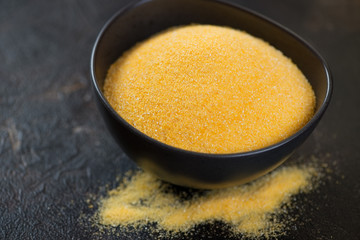 Bowl of raw polenta over dark brown stone background, selective focus