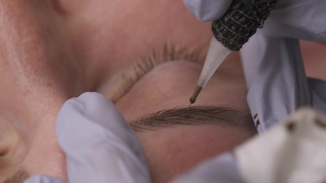 Close-up demonstration video of eyebrows micropigmentation procedure. Skilled cosmetologist doing eyebrows permanent make-up.