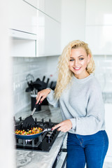Fototapeta na wymiar Young pretty blonde woman cooking dinner on the kitchen