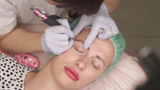 Cosmetic procedure of eyebrows permanent make-up. A top shot of a professional cosmetologist performing eyebrows micropigmentation procedure