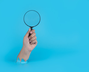 hand holding a magnifying glass through the torn blue plastic background