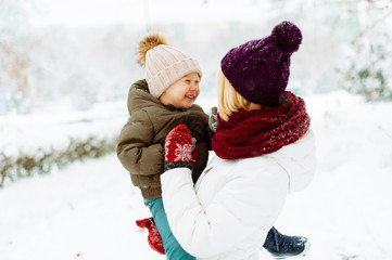 Photo of a handsome mother hugging her little boy, having time together in a winter walk