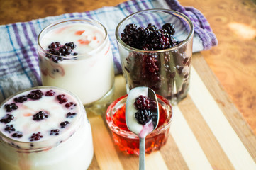 Yogurt in transparent jars with fresh blackberry and strawberry voyen with a spoon, on wooden background