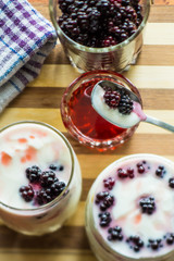 Yogurt in transparent jars with fresh blackberry and strawberry voyen with a spoon, on wooden background