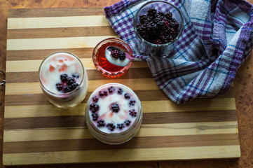 Yogurt in transparent jars with fresh blackberry and strawberry voyen with a spoon, on wooden background