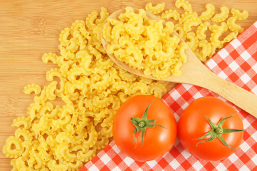 Macaroni on wooden and tablecloth background with spoon and tomatoes