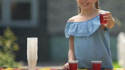 Joyful girl showing juice plastic glass, selling refreshing syrup outdoors drink