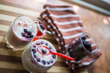 Yogurt in transparent jars with fresh blackberry and strawberry voyen with a spoon, on wooden background