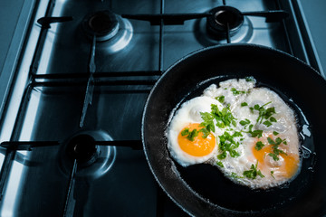 Sunny side up fried eggs with parsley decoration on cast iron frying pan on kitchen stove. Concept of home made cuisine or healthy food with protein nutrition. Close up image with partially soft focus