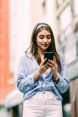 Fototapeta premium Young woman walking and using a smart phone in the street in a sunny summer day