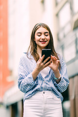 Fototapeta premium Happy woman uses a smart phone standing in the street