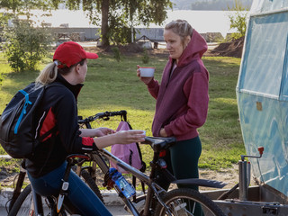 Two young girls in sportswear are resting after a bike ride. They drink tea, laugh and talk.